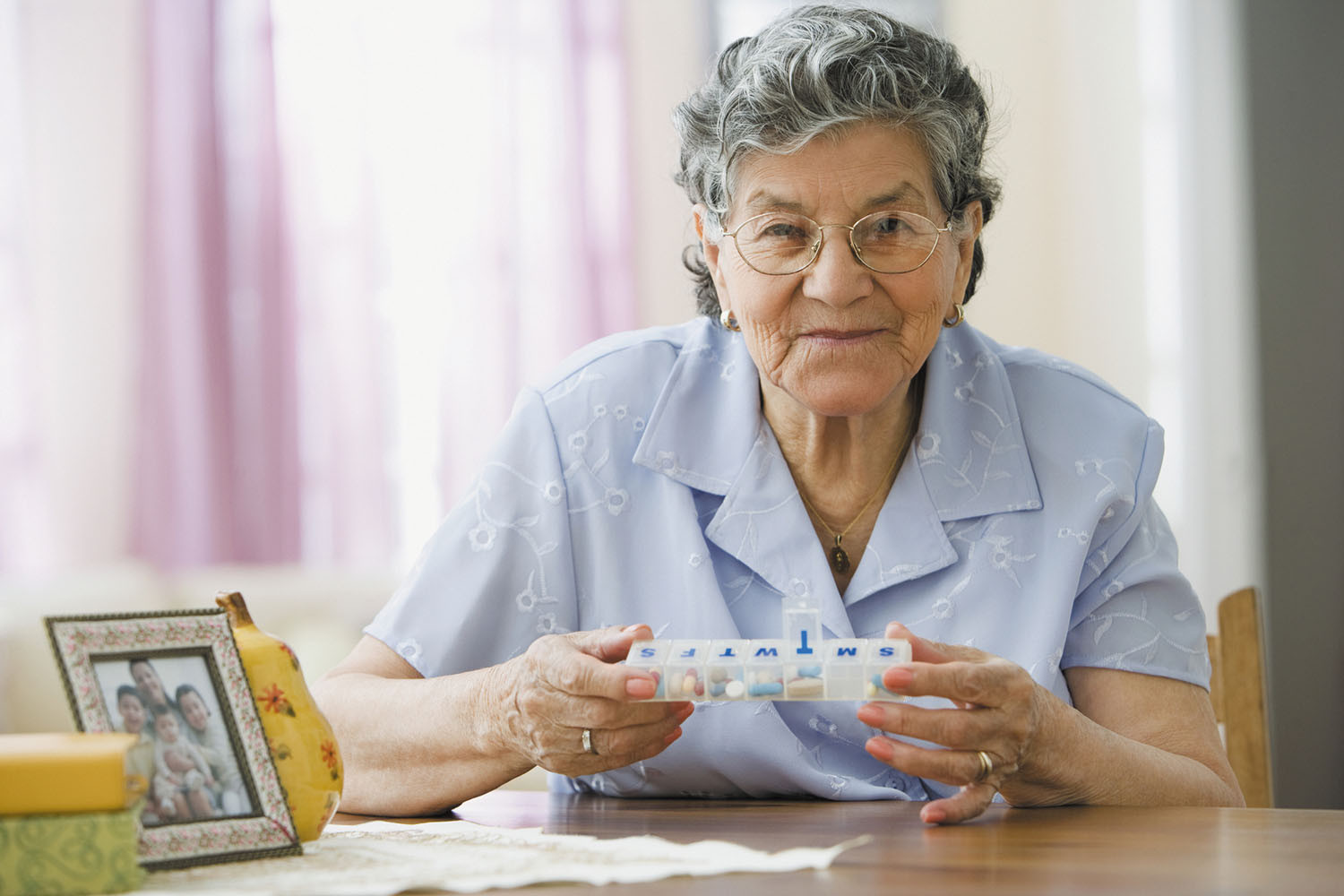 photo of a senior woman holding a seven-day pill container with one compartment open