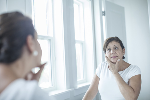 photo of a middle-age woman looking at herself in a mirror, holding one hand under her chin so her fingers are on one cheek