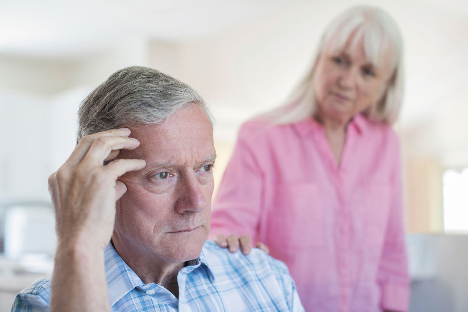 photo of a senior couple, the man is holding a hand to the side of his head and looks confused; the woman looks at him with concern