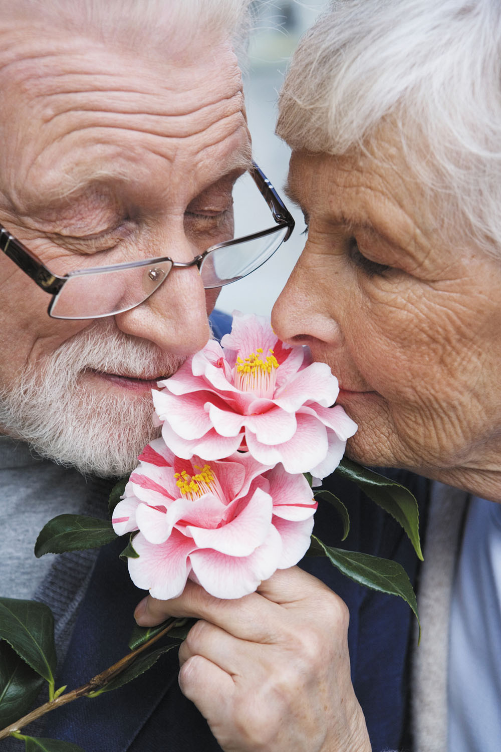 photo of a senior man and woman standing close together and smelling flowers held by the woman