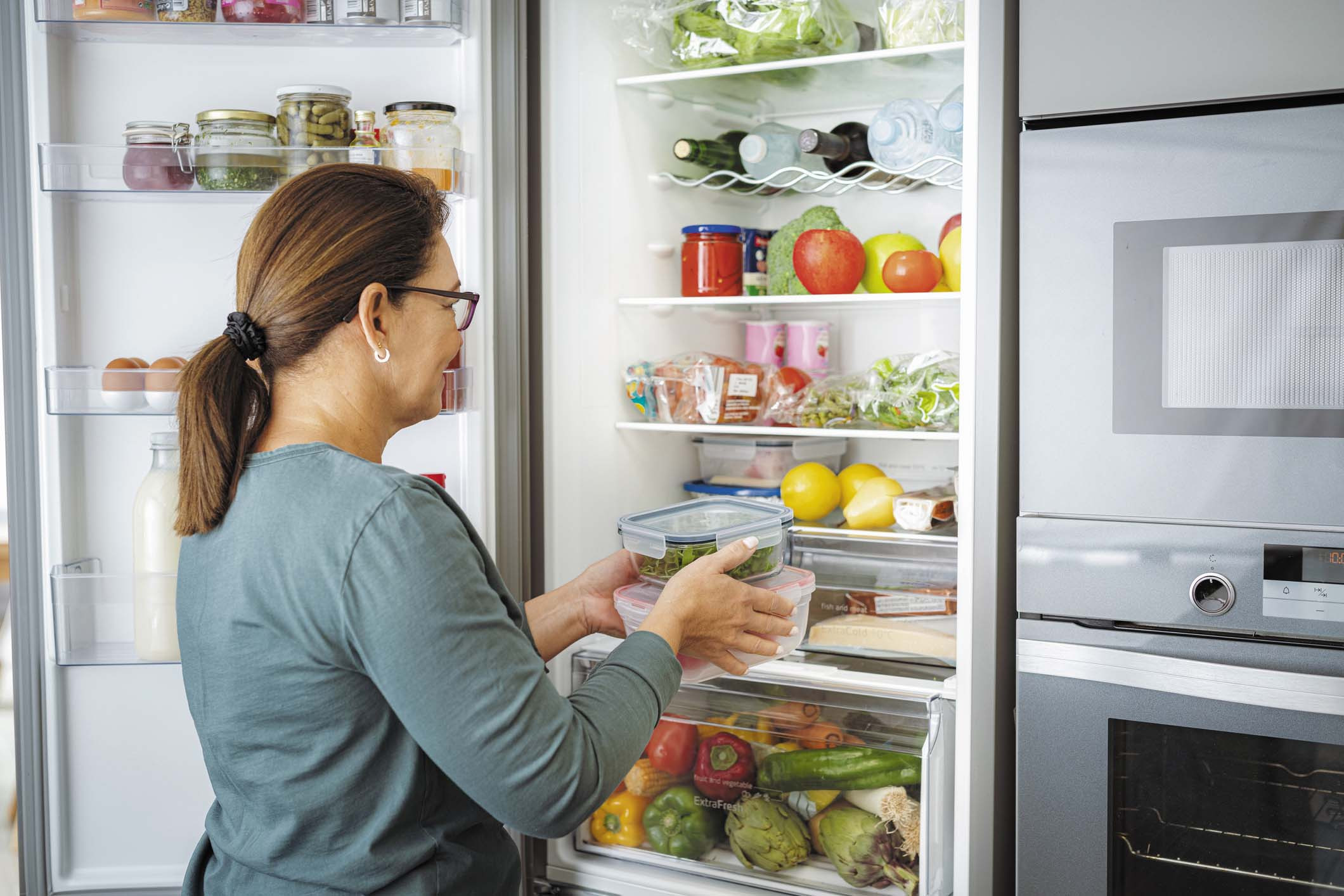 photo of a woman viewed from behind as she is putting food containers into her refrigerator