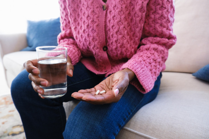 cropped photo showing the torso and hands of a person holding a glass of water in one hand and two pills in the other