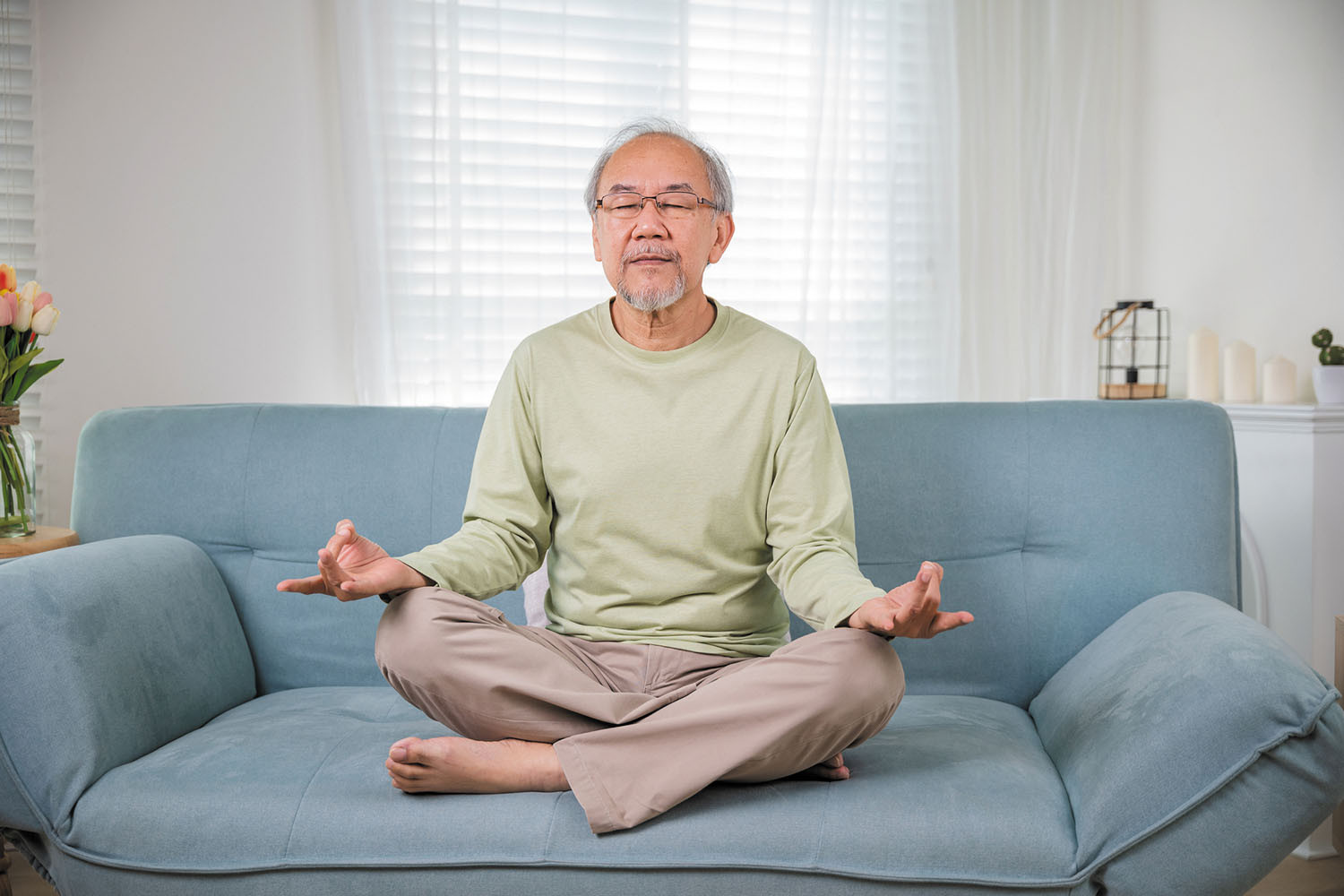photo of a mature man meditating while sitting in the lotus position on a couch