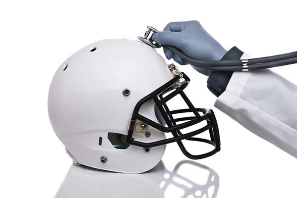 photo d'un casque de football blanc et d'un bras avec une blouse blanche et un gant de protection sur la main tenant un stéthoscope sur le haut du casque