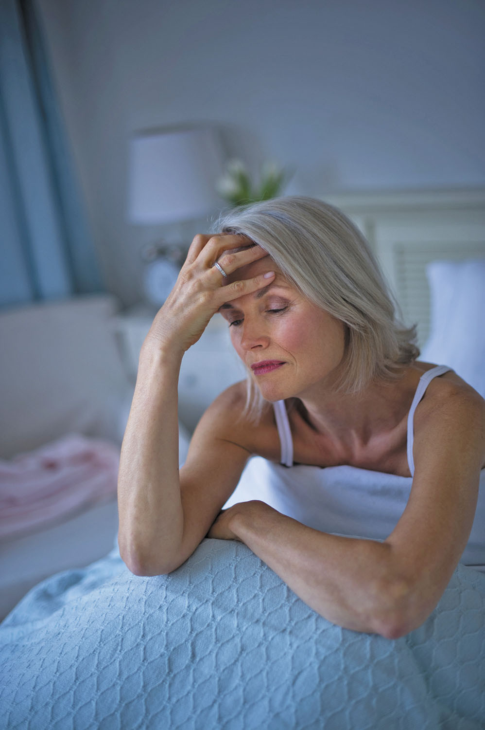 photo of a woman sitting up in bed holding her hand to her forehead, looking distressed because she can't fall asleep