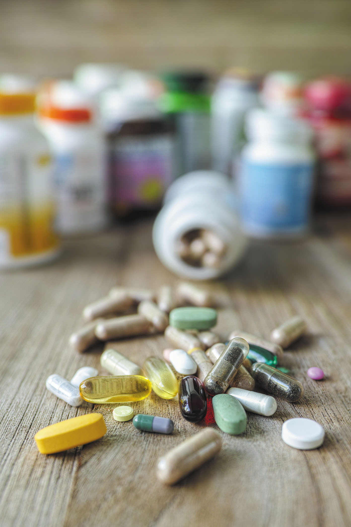 photo of an assortment of pills on a table with several bottles out of focus in the background, one lying on its side