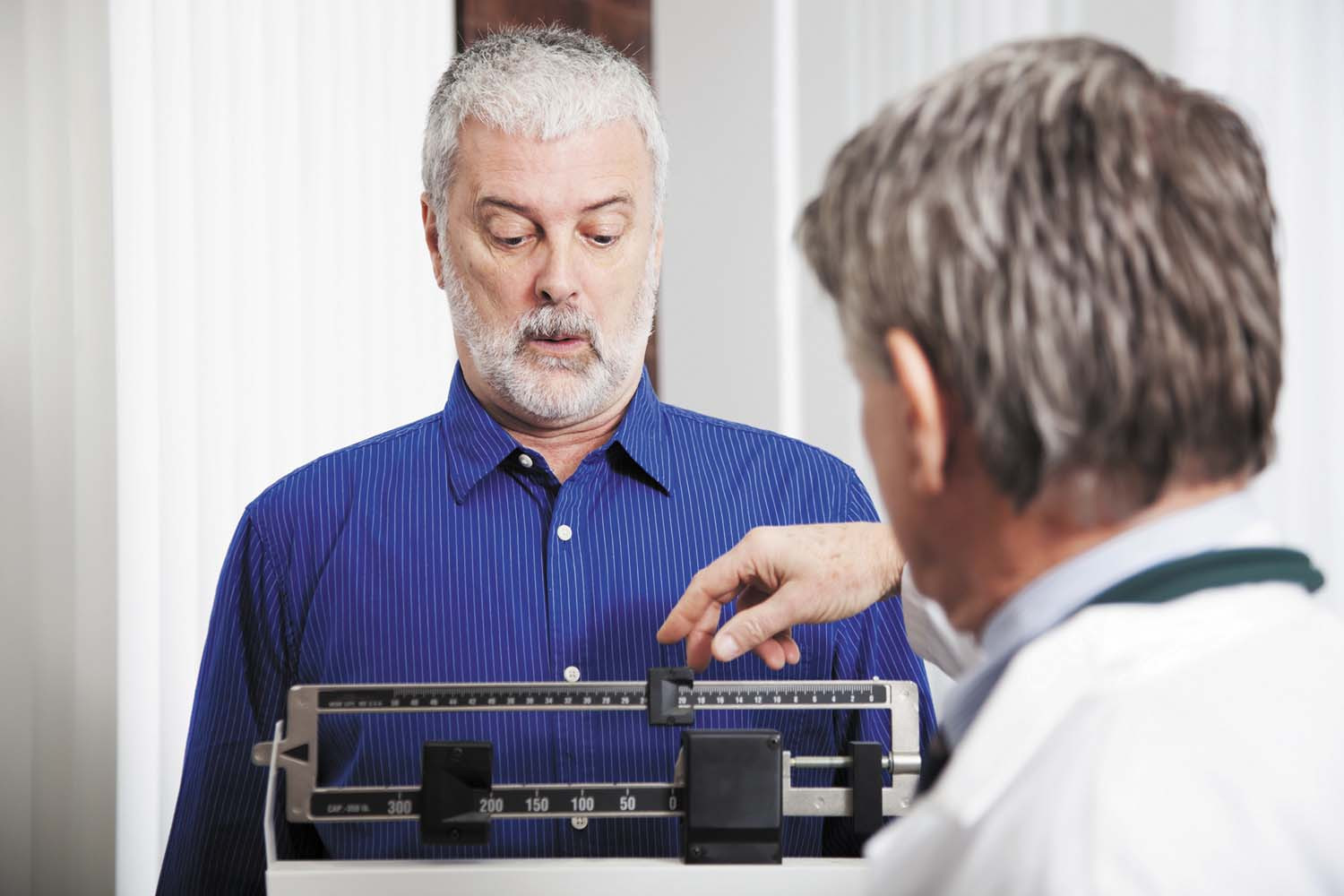 photo of a man being weighed at a doctor's office using the type of scale with sliding markers that have to be balanced