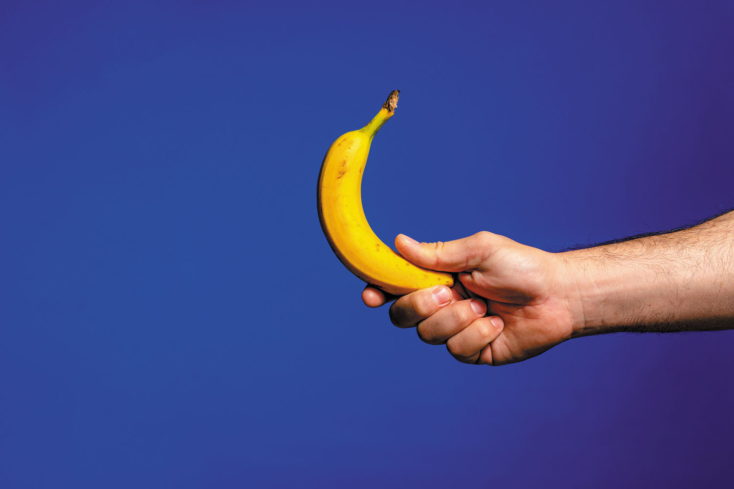 photo of a hand holding a banana against a dark blue background