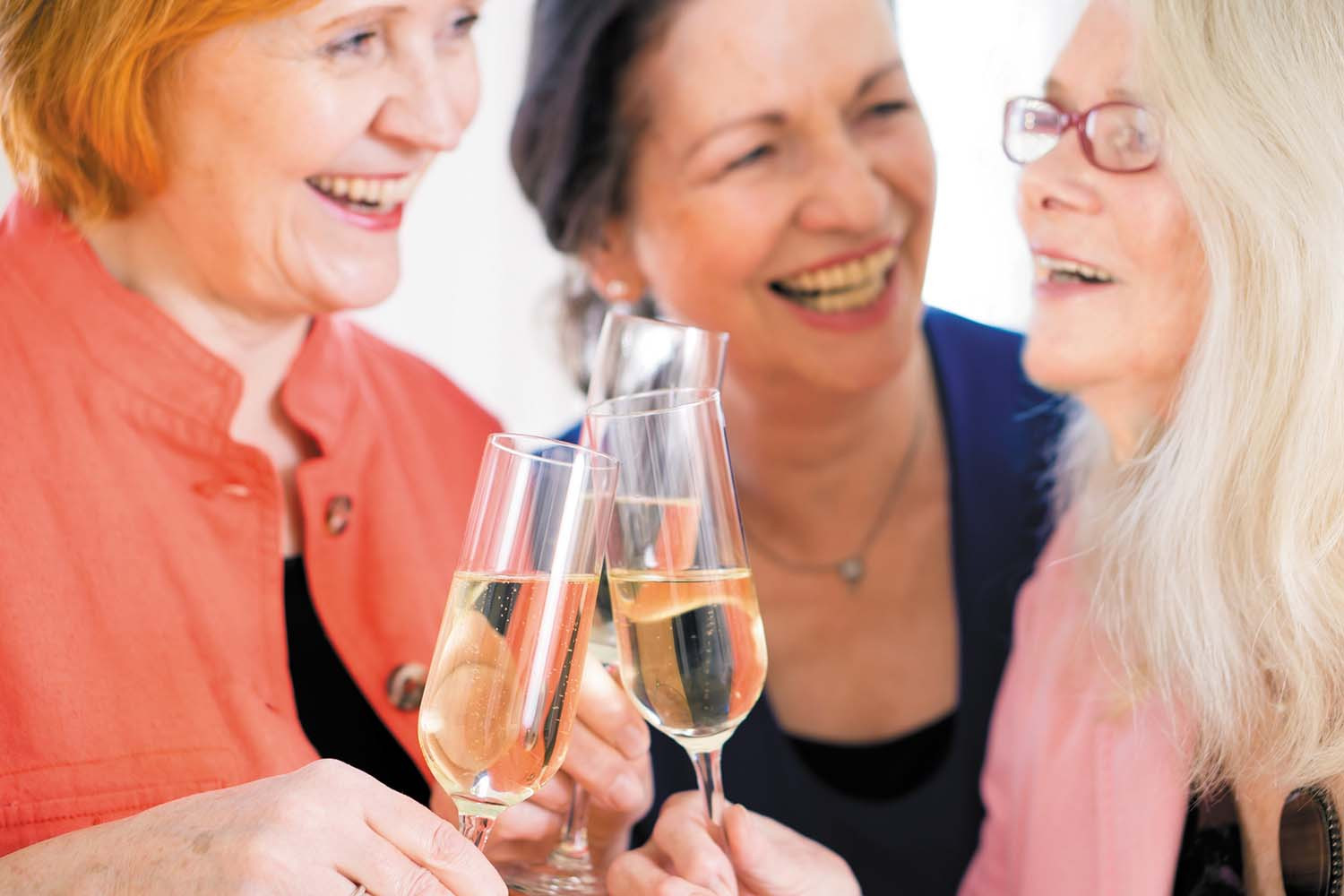 photo of a group of three women smiling while toasting with glasses of red wine