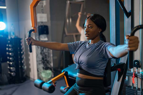 photo of a woman using an exercise machine in a gym to work her arm and chest muscles