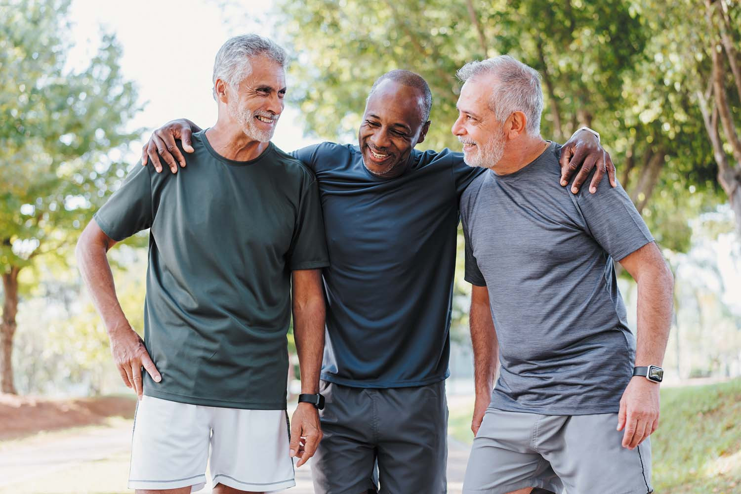 photo of three mature men standing together in exercise clothing; background looks like a park