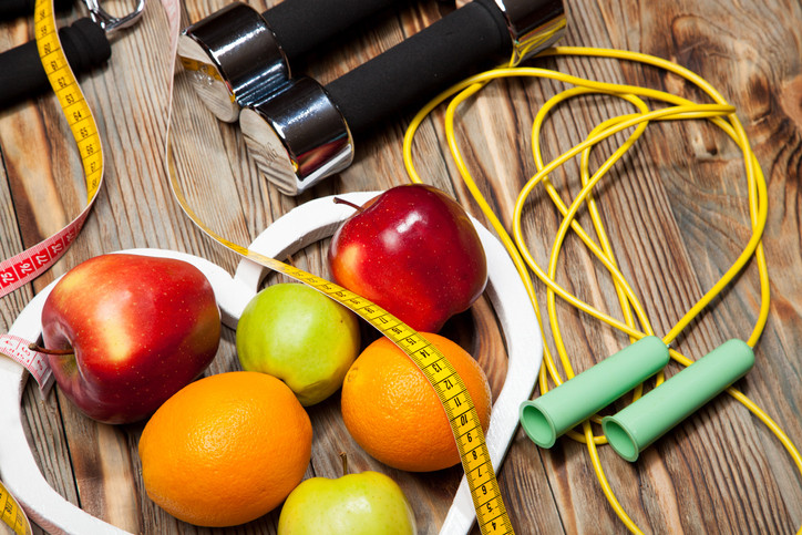 photo of a small grouping of fruits inside a white heart shape on a wooden table, next to a jump rope, hand weights, and a tape measure