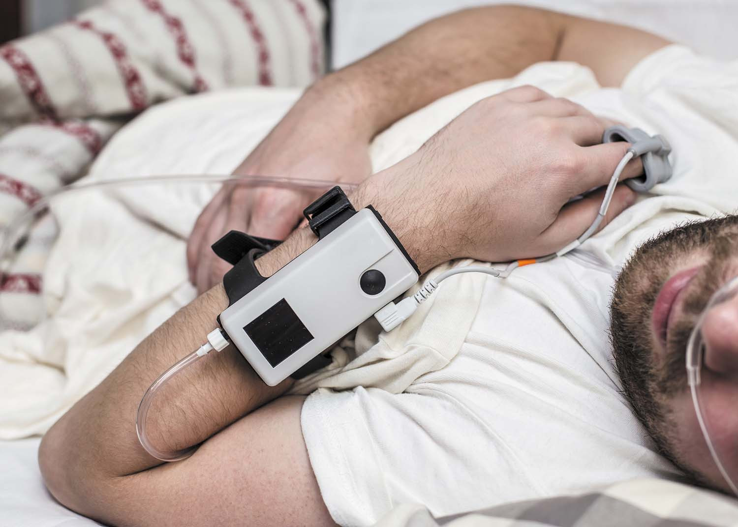 photo of a man sleeping while taking a sleeping test; a device attached to his wrist that records data while he sleeps
