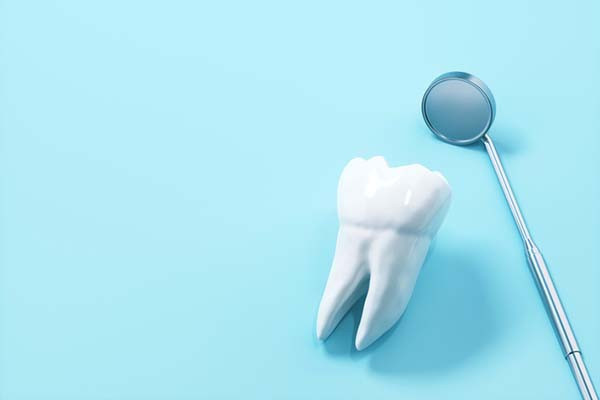 image of a human tooth lying next to a dental mirror on a blue background