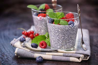 photo of two glasses of chia pudding topped with fresh berries and mint, placed on a folded striped cloth napkin