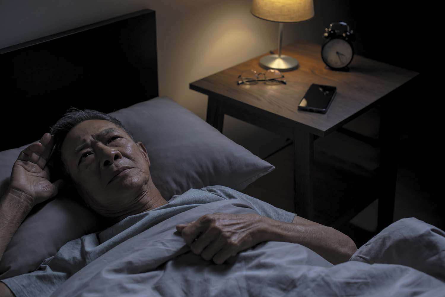 photo of a man in bed, lying on his back unable to sleep