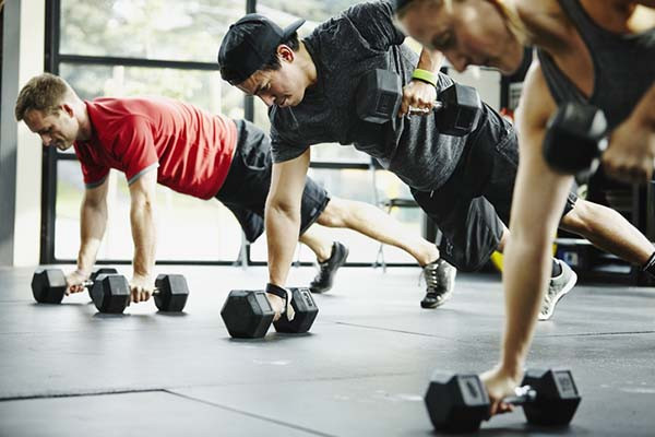 photo of three men doing modified push-up exercises with hand weights in a gym