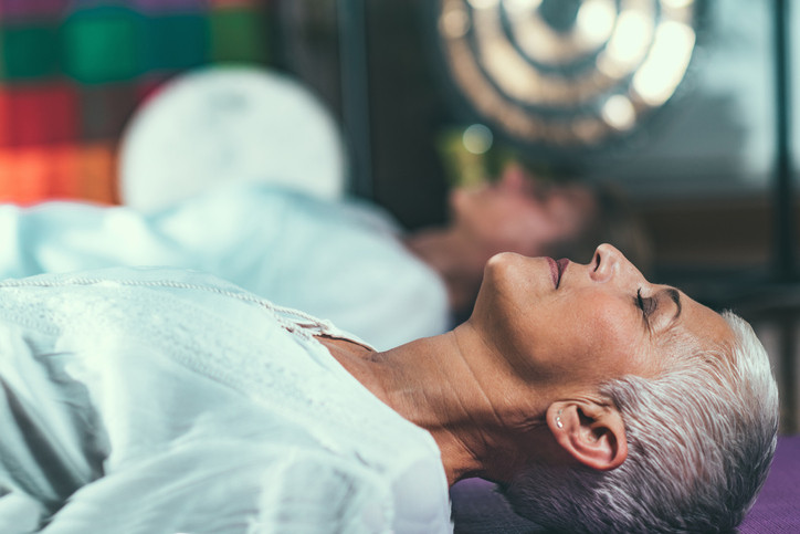 photo of a woman lying on her back while meditating, in a relaxed position with her eyes closed