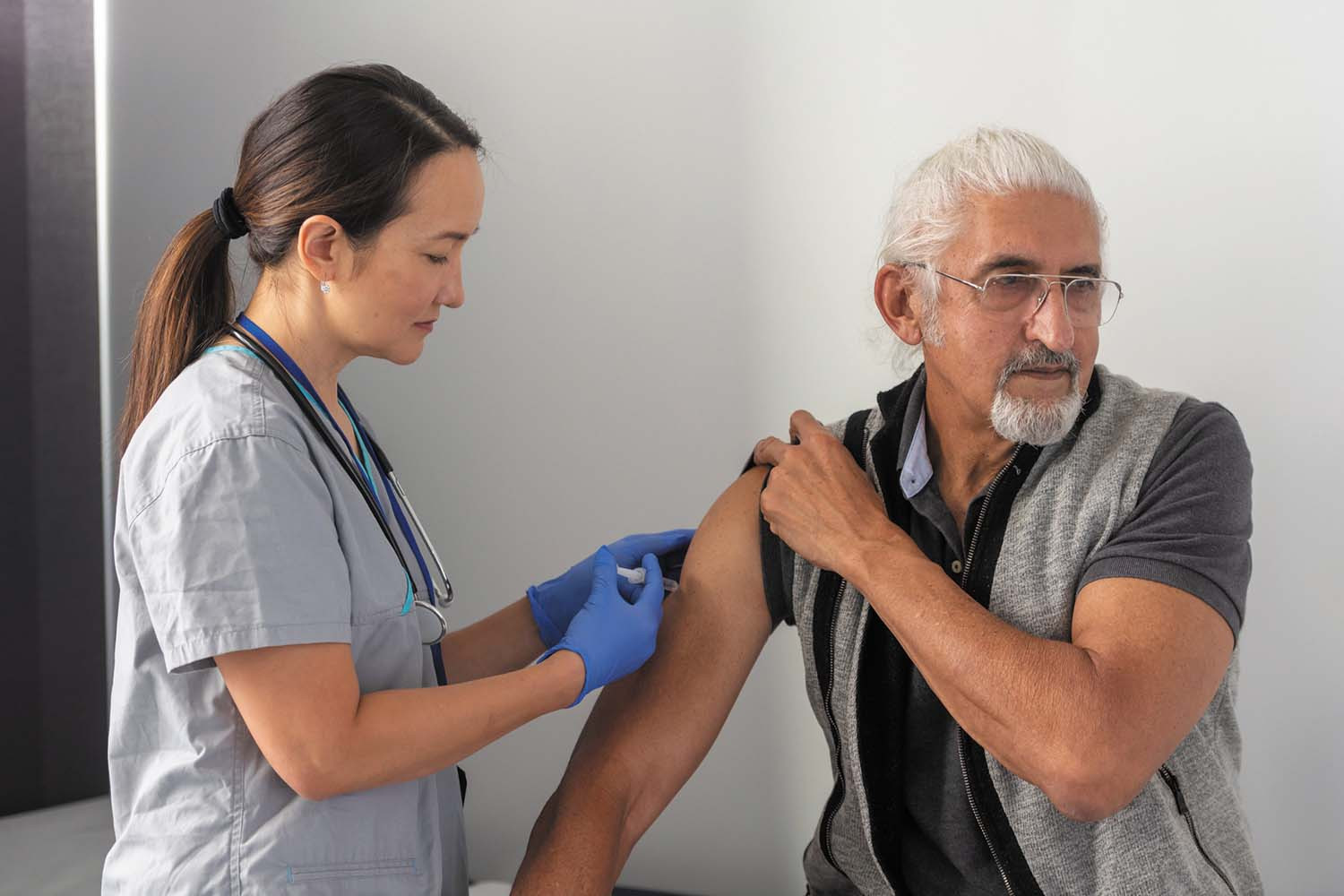 photo of a senior man receiving an injection in his upper arm from a health care worker