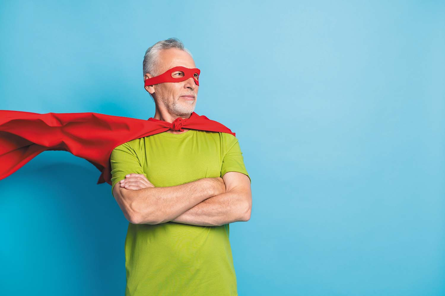 photo of a mature man wearing a superhero-style cape and a mask around his eyes; he is standing with his arms crossed