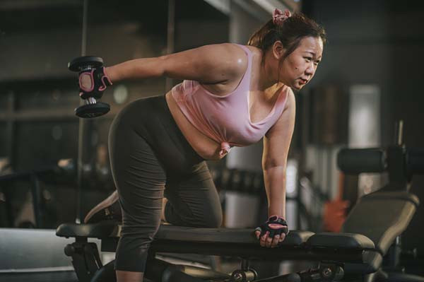 photo of a woman exercising with dumbbells in a gym while supporting herself on a weight bench