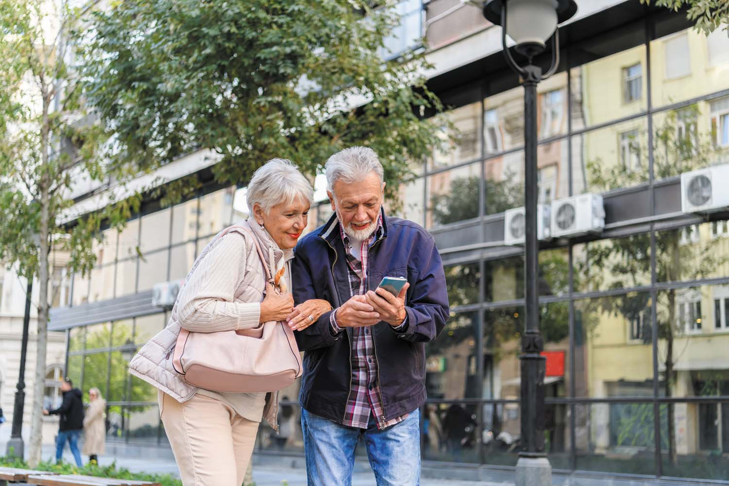 photo of a senior couple looking at a smartphone while standing outside a building