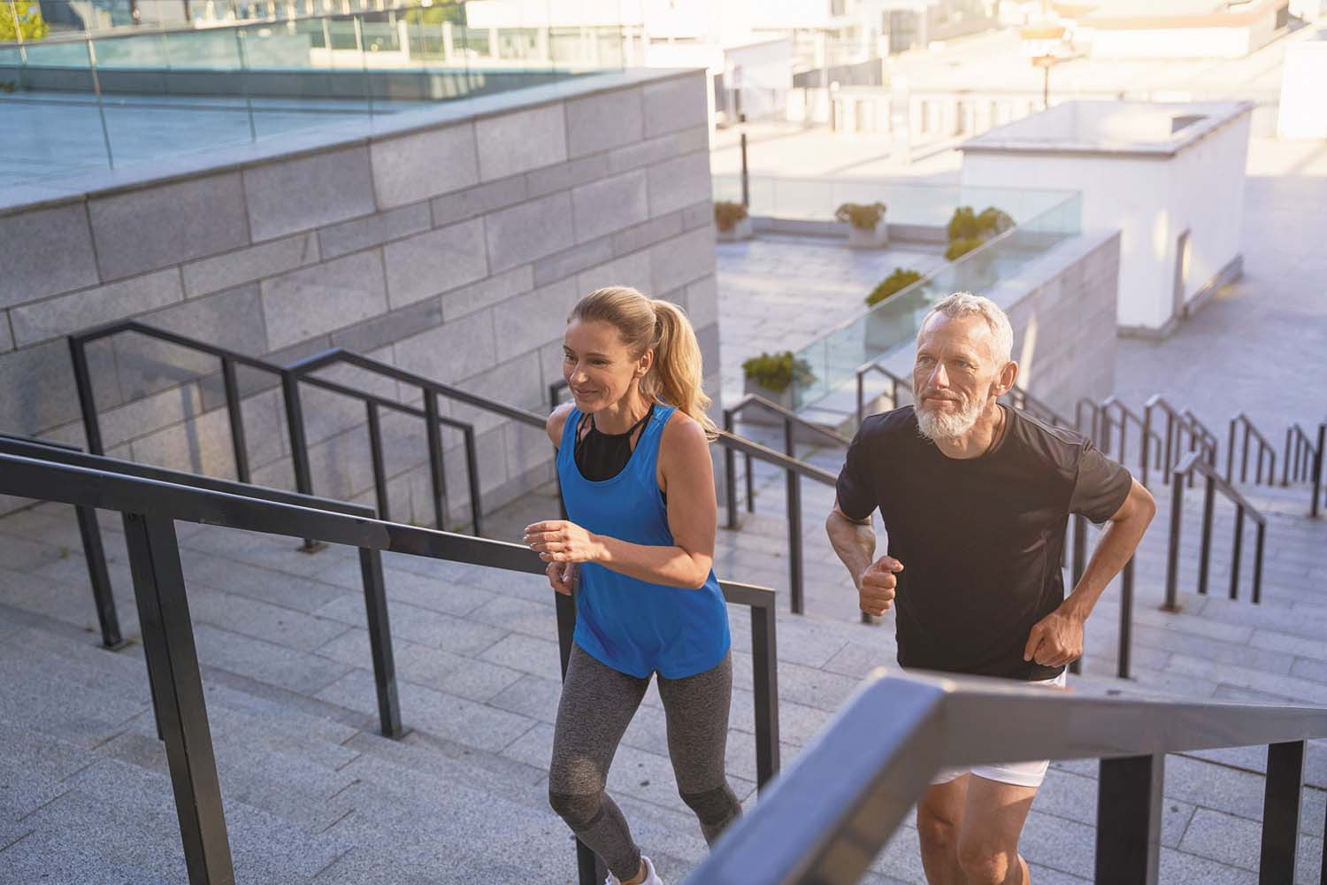 photo of a woman and a man exercising by running up stairs from an outdoor plaza