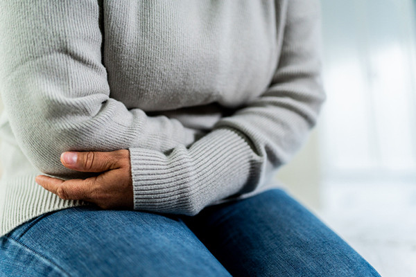 cropped photo showing the torso of a woman who has her arms crossed in front of her stomach, indicating digestive distress