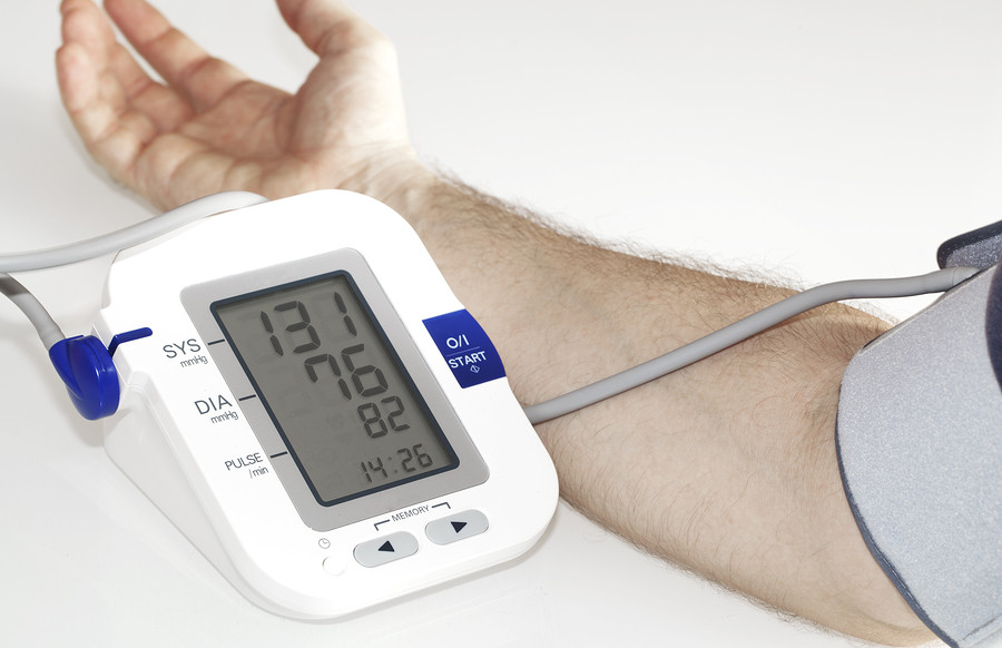 cropped photo showing a person's arm with a blood pressure cuff attached, and a device showing the numbers on an LCD screen