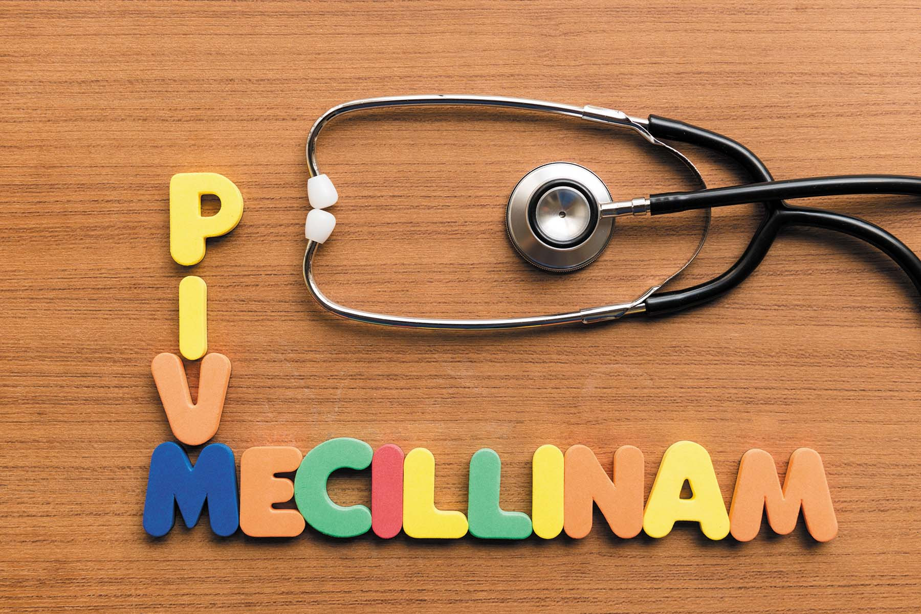 photo illustration of letters spelling out pivmecillinam on a wood table next to a stethoscope