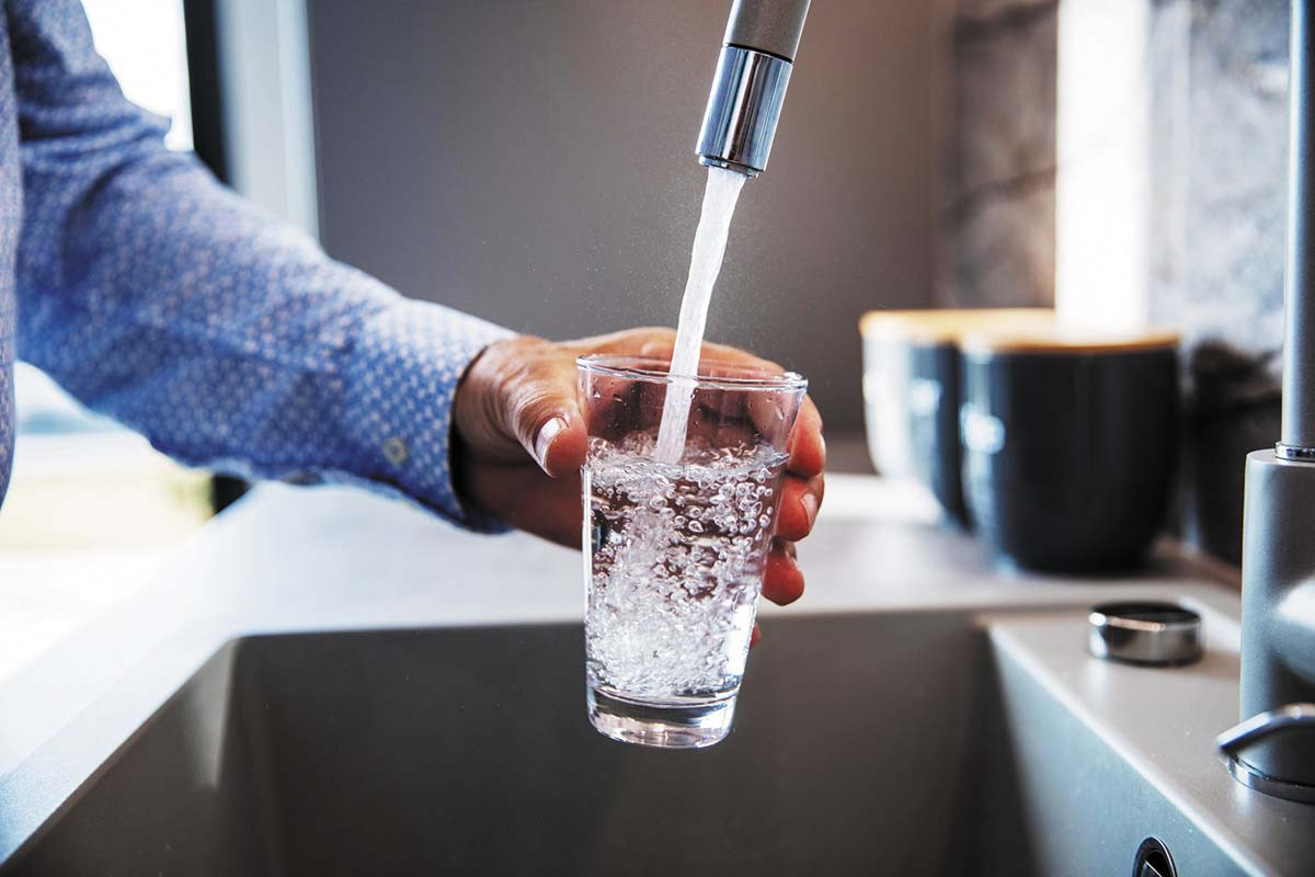 cropped photo showing the arm of a person filling a glass of water under a running tap