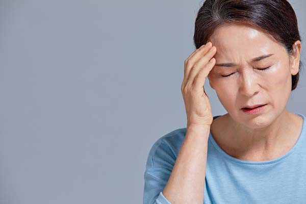 photo of a woman holding with her eyes closed, her hand to her forehead due to headache pain