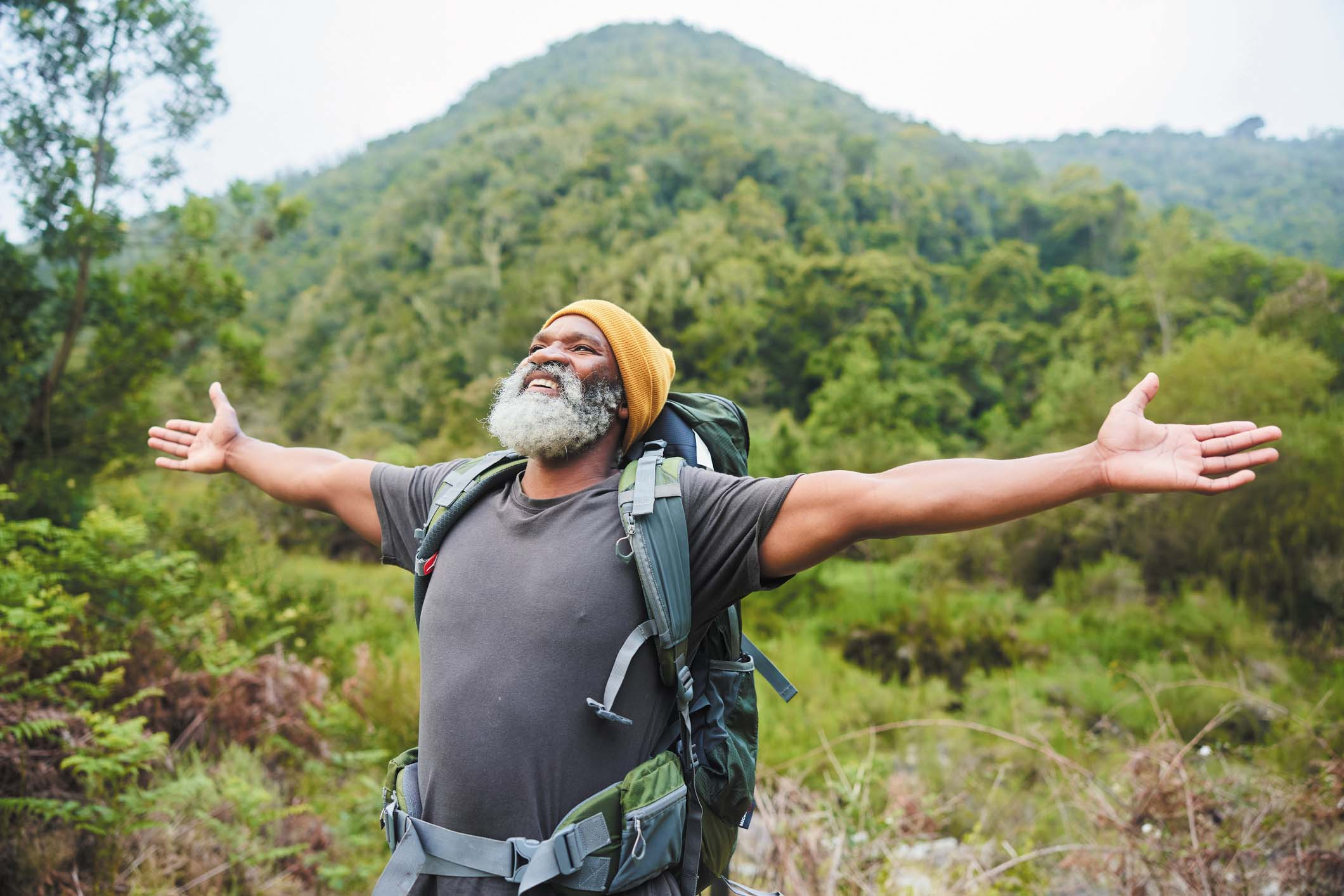 photo of a senior man on a hike standing with his arms outstretched, celebrating the experience and being in the outdoors