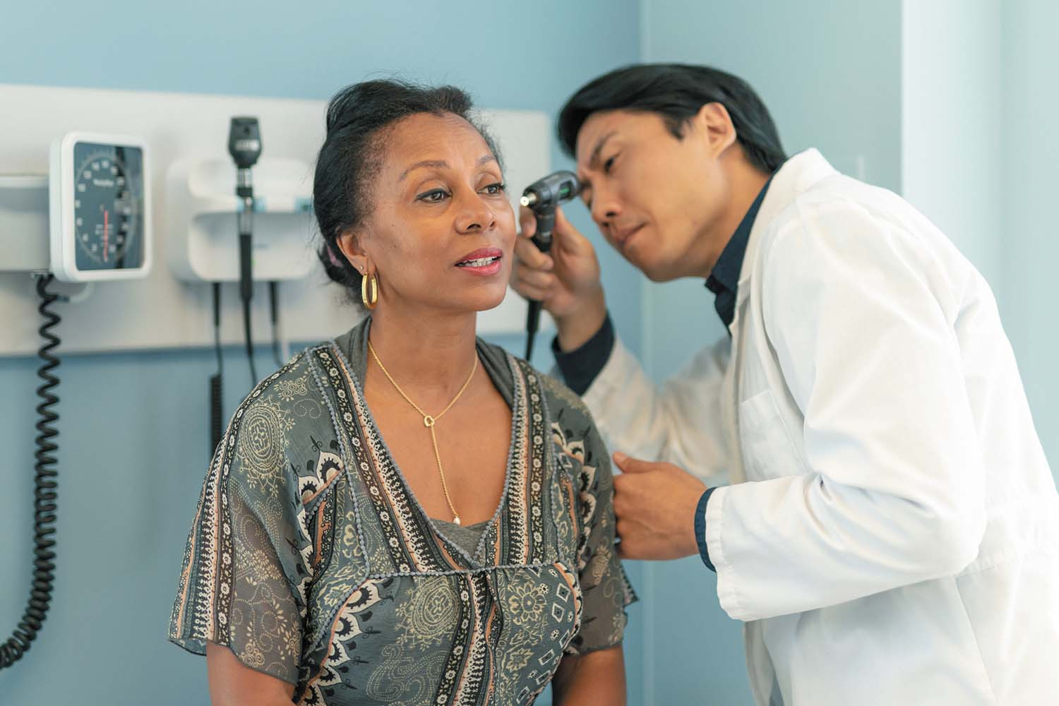 photo of a woman having her ear examined by a doctor, who is looking into her ear canal with a lighted scope