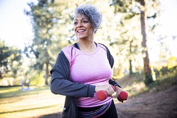 photo of a mature woman walking outdoors while holding hend weights