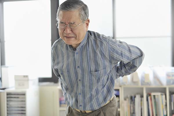 photo of a senior man grimacing in pain and holding his hands behind him, suggesting back pain