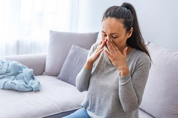 photo of a woman with a sinus headache, she is holding her hands to the sides of her nose due to sinus pain