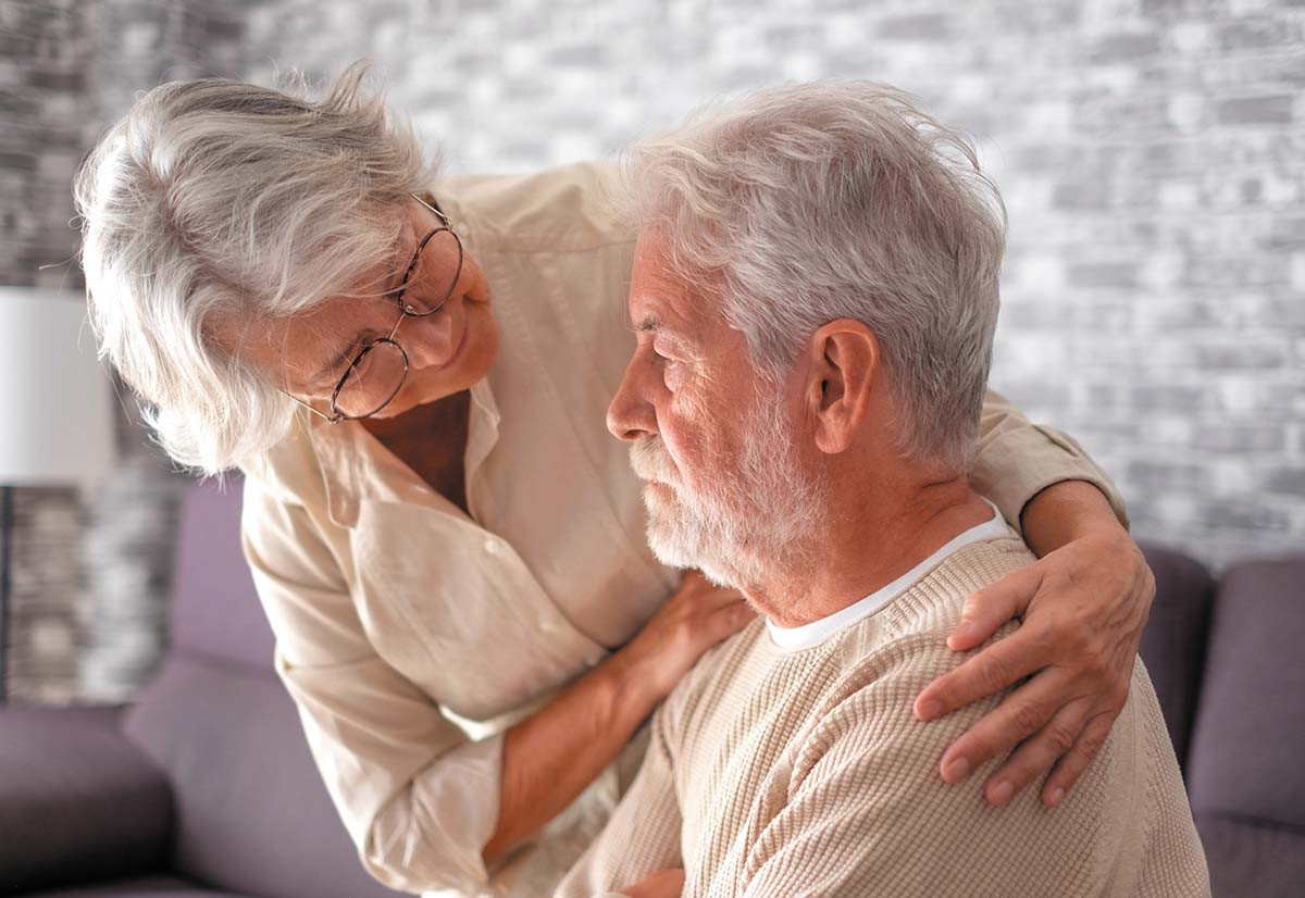 photo of a senior woman comforting her husband while providing care for him