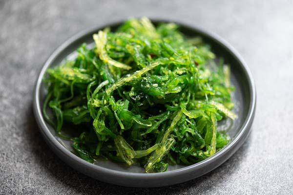 photo of fresh green seaweed served on a gray plate on a dark surface