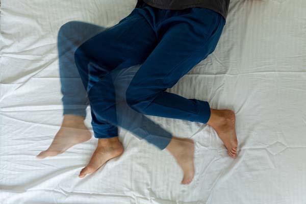 photo showing the lower half of a person's body in a bed viewed from above; the legs are shown in multiple positions, suggesting restless legs syndrome