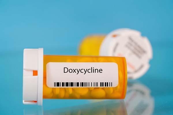 photo illustration of an orange medication bottle on its side, with a label showing a bar code and the word doxycycline; another medication bottle is behind it, out of focus