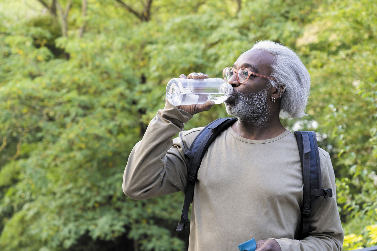 photo of a man outdoors drinking from a water bottle while hiking