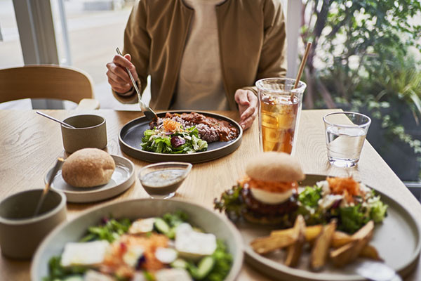 photo looking across a table at a cafe, table holds several vegan dishes and glasses of water and iced tea