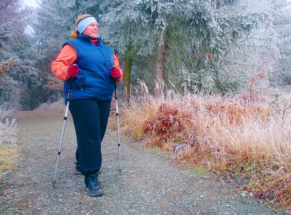 Kobieta ubrana ciepło warstwowo i chodząca w zimnym krajobrazie przy użyciu kijków nordyckich