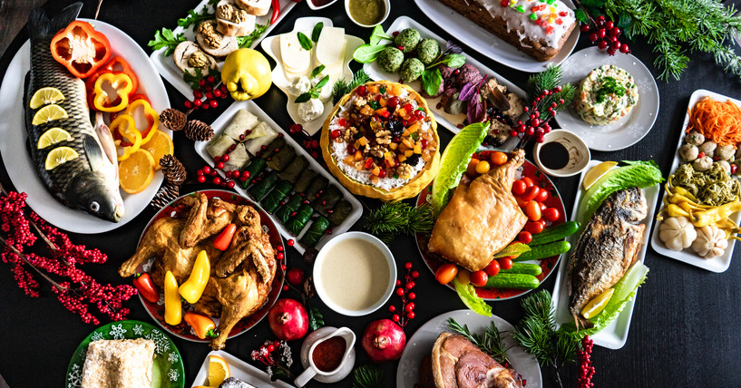 A table laden with festive foods: whole fish with lemon wedges, browned chicken, ham, colorful vegetables, pies, blintzes and more