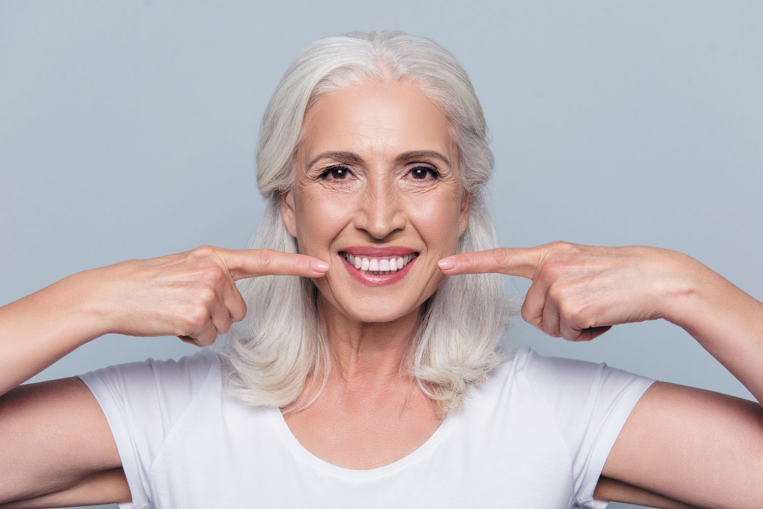 photo of a mature woman pointing to her smile with both hands