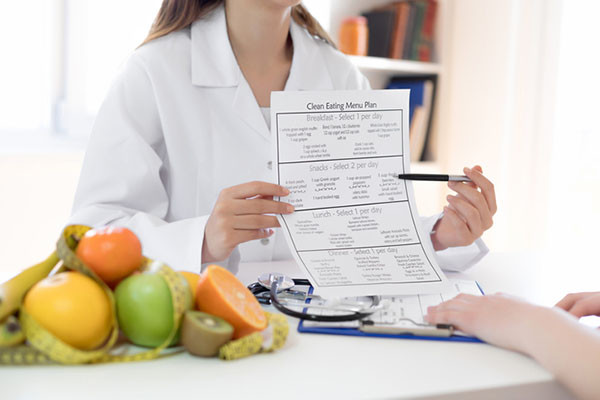 cropped photo showing the torso of a nutritionist sitting at a desk holding up a nutrition plan and pointing to it with a pen