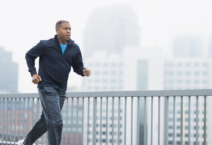 A middle-aged man wearing a blue zip top and lighter blue track pants running alongside a blurred cityscape